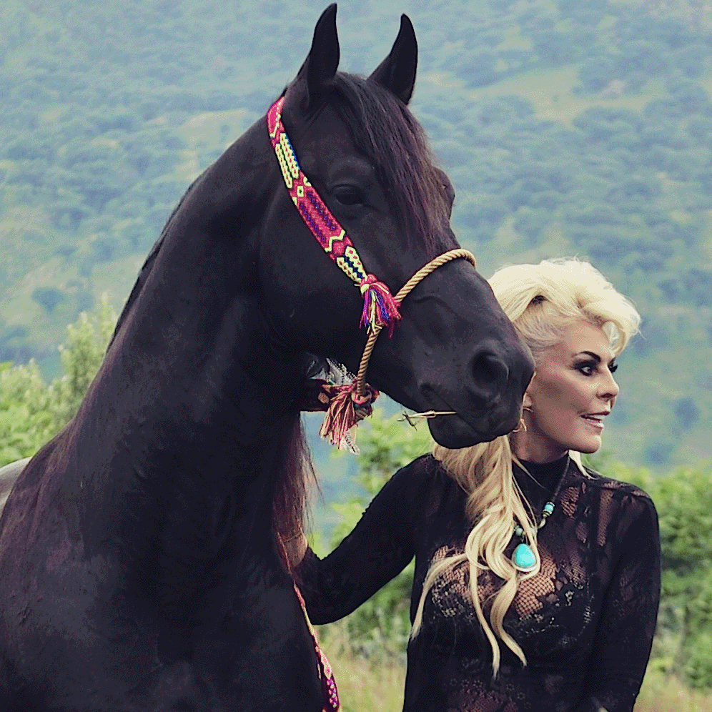 Woman standing next to a horse in a scenic outdoor setting with mountains and plants.